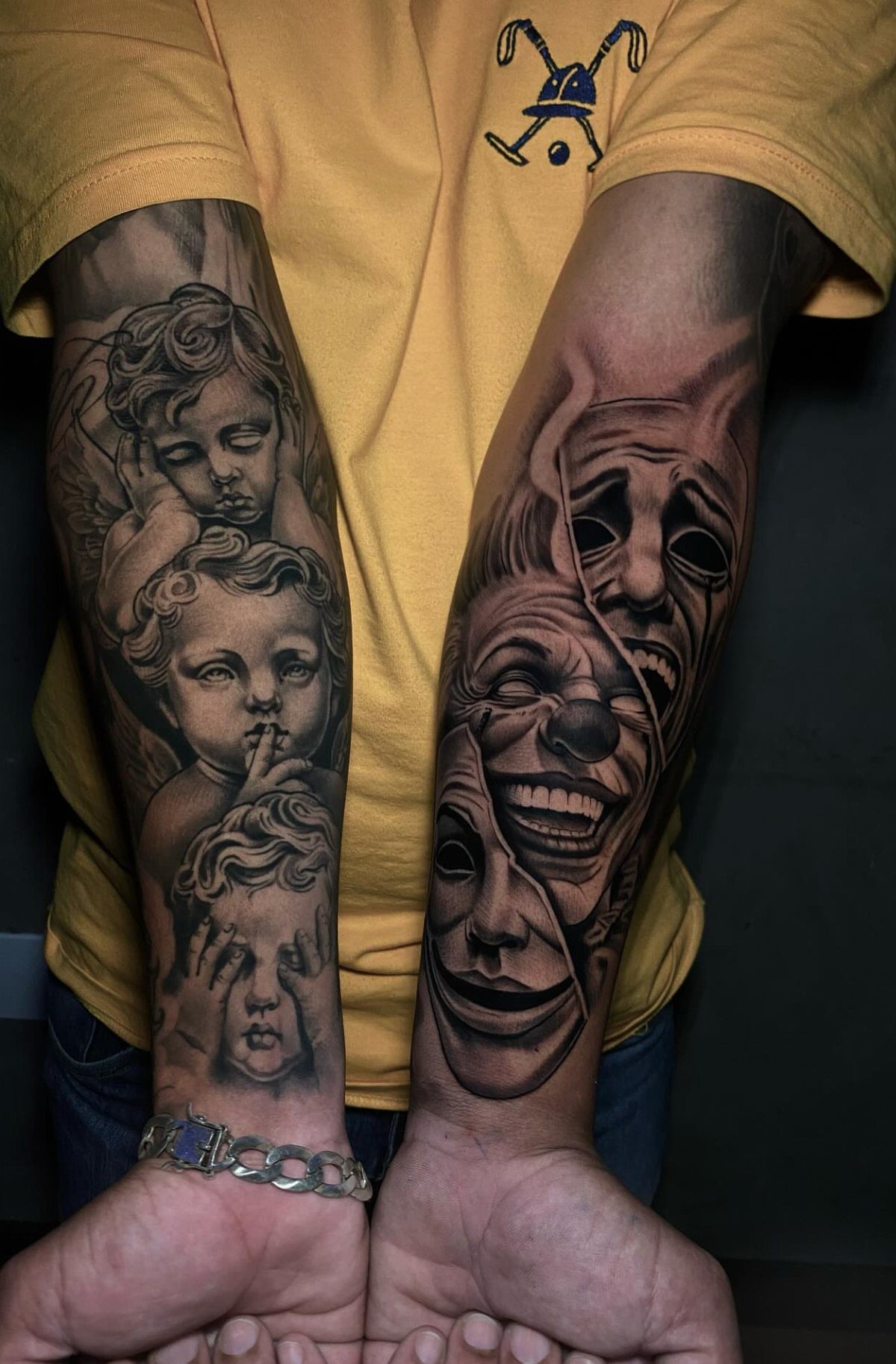 Forearms with black and grey realism tattoos of cherubs and theatrical masks