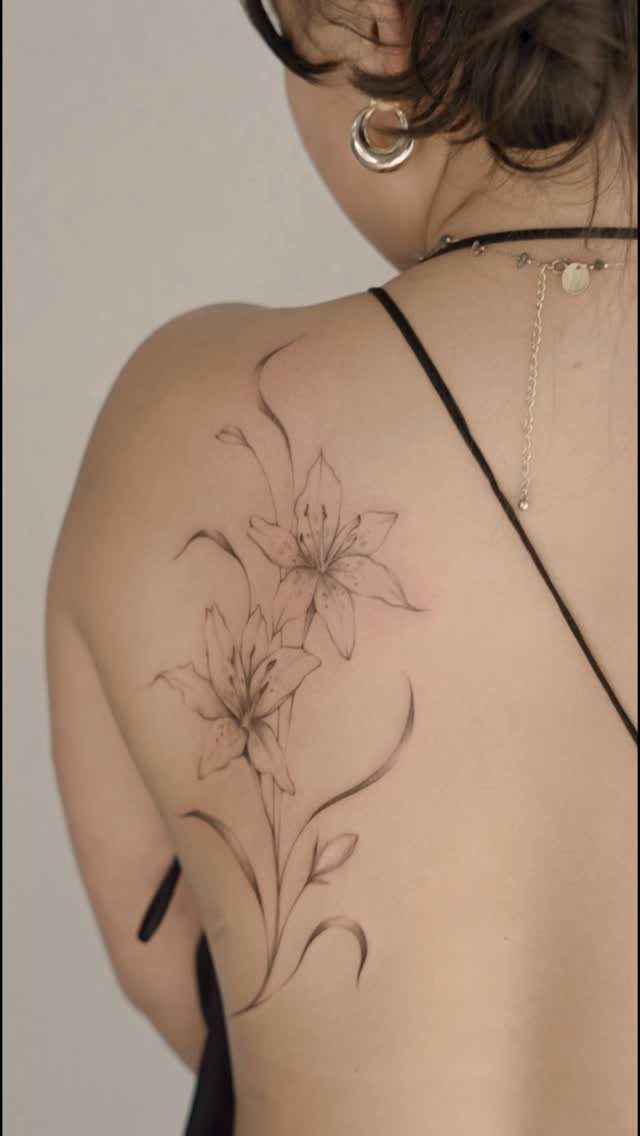 Lily flower tattoo with thin black lines on a person's upper back and shoulder