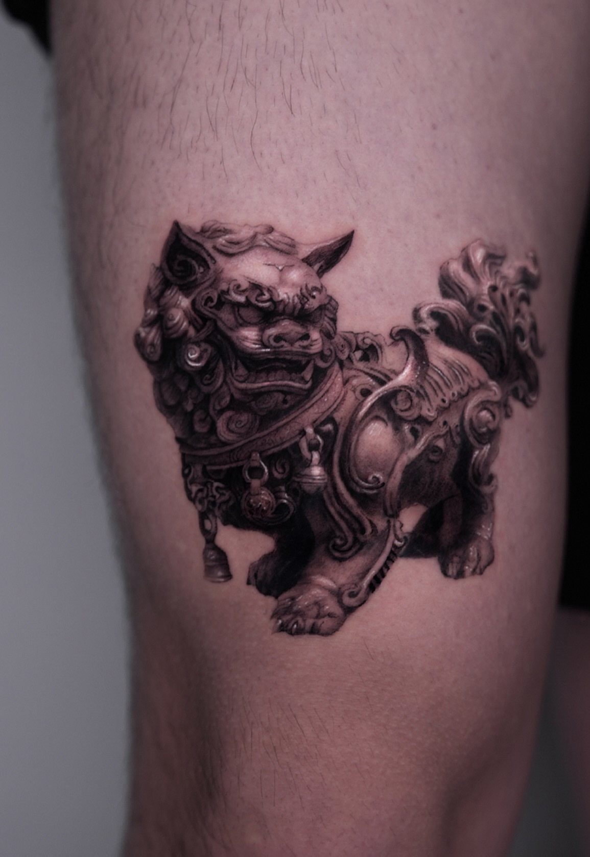 Detailed black and grey realism tattoo of a Chinese guardian lion on a leg.