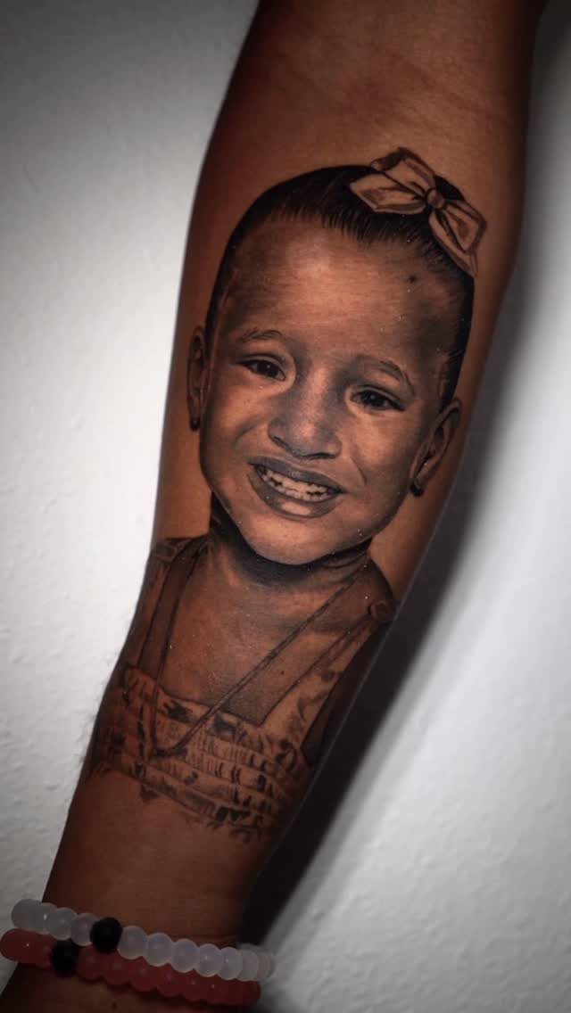 Detailed black and grey realism portrait tattoo of a young girl on a forearm.