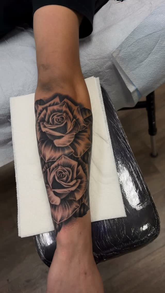 Two photorealistic black and grey rose tattoos on a person's forearm.