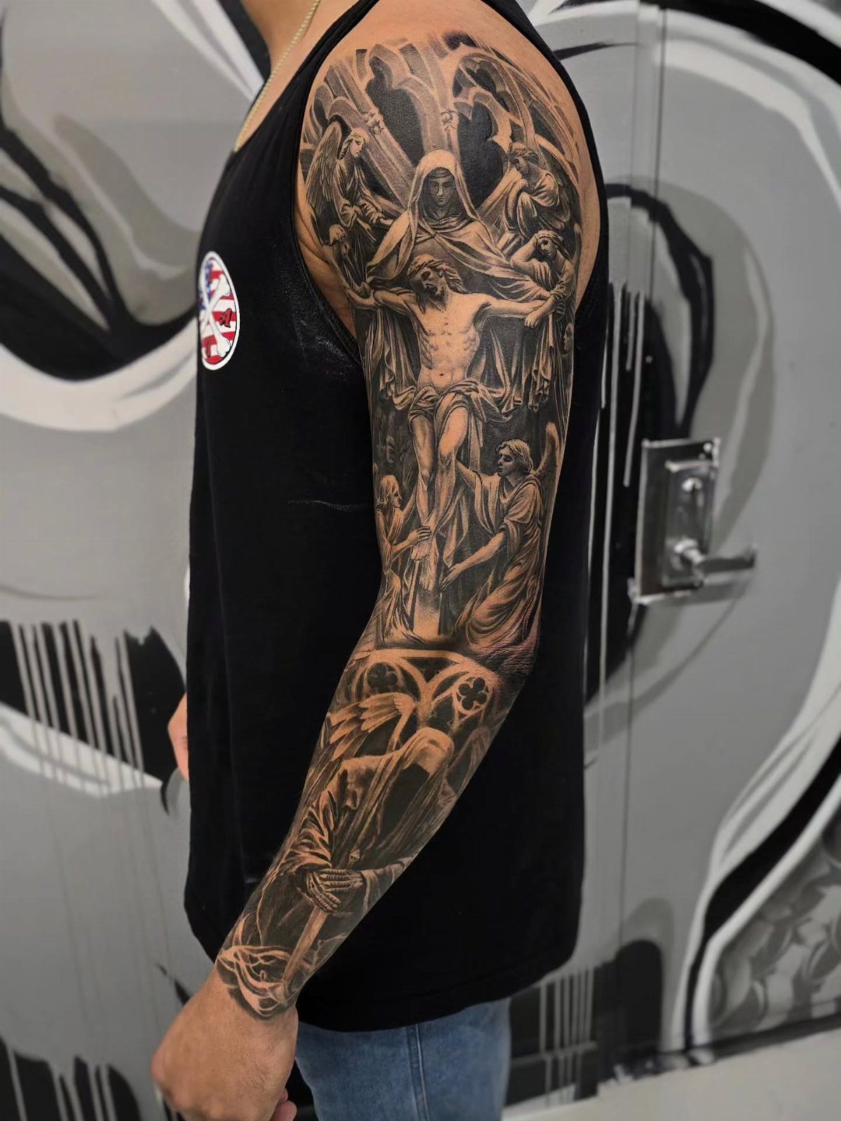 Full sleeve black and grey realism tattoo depicting Jesus on the cross and religious figures.