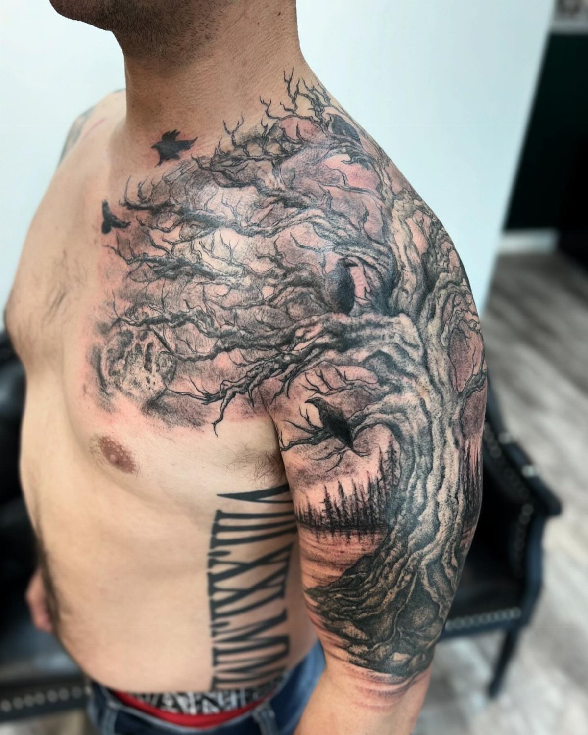 Black and grey tattoo of a gnarled tree and forest landscape on a man's arm.
