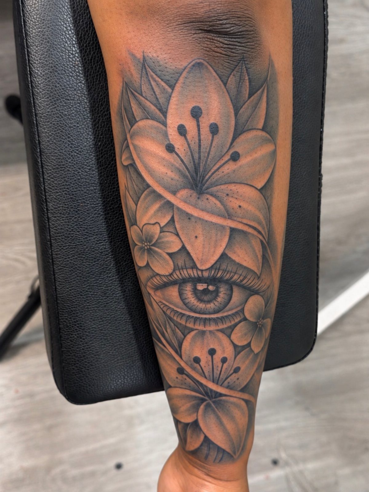 Black and grey tattoo of a lily and an eye on a forearm