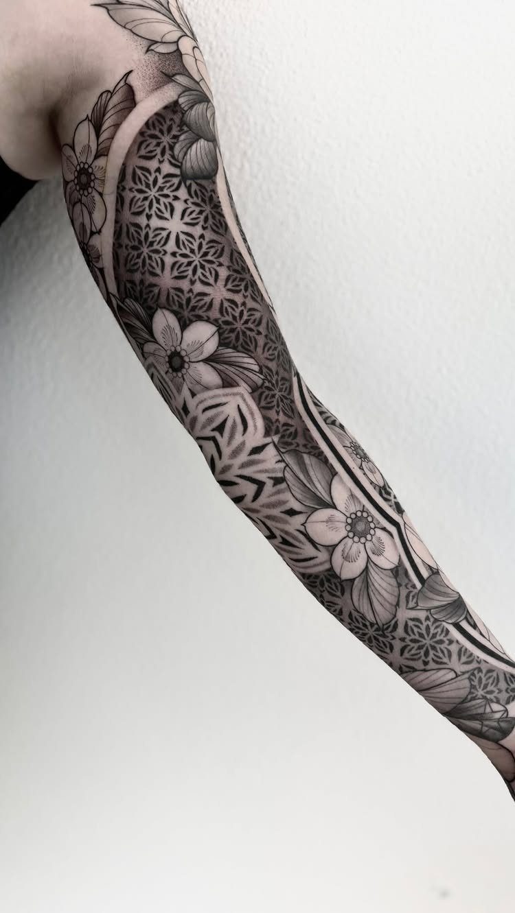 Geometric and floral black and grey tattoo covering a person's forearm