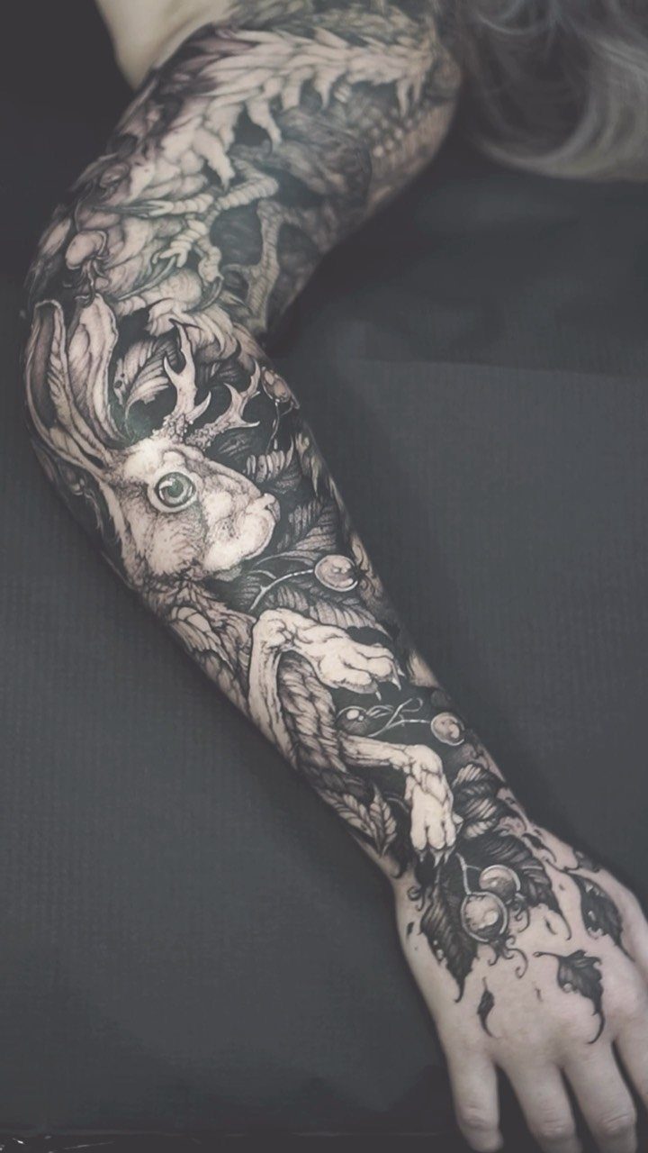 Detailed black and grey sleeve tattoo featuring a rabbit with antlers and forest elements.