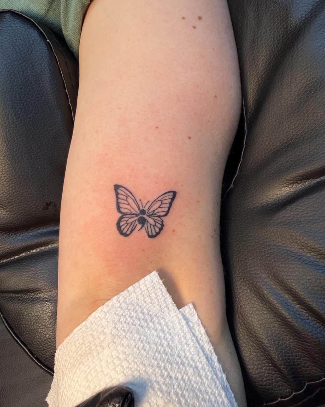 Small black butterfly semicolon tattoo on a person's forearm.
