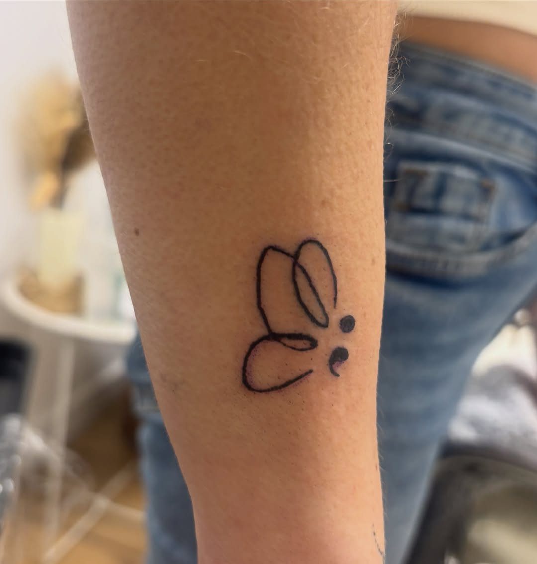 Butterfly semicolon tattoo with minimalist line art on a person's forearm