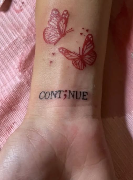 Red butterfly tattoos and the word CONTINUE with a semicolon on a wrist.