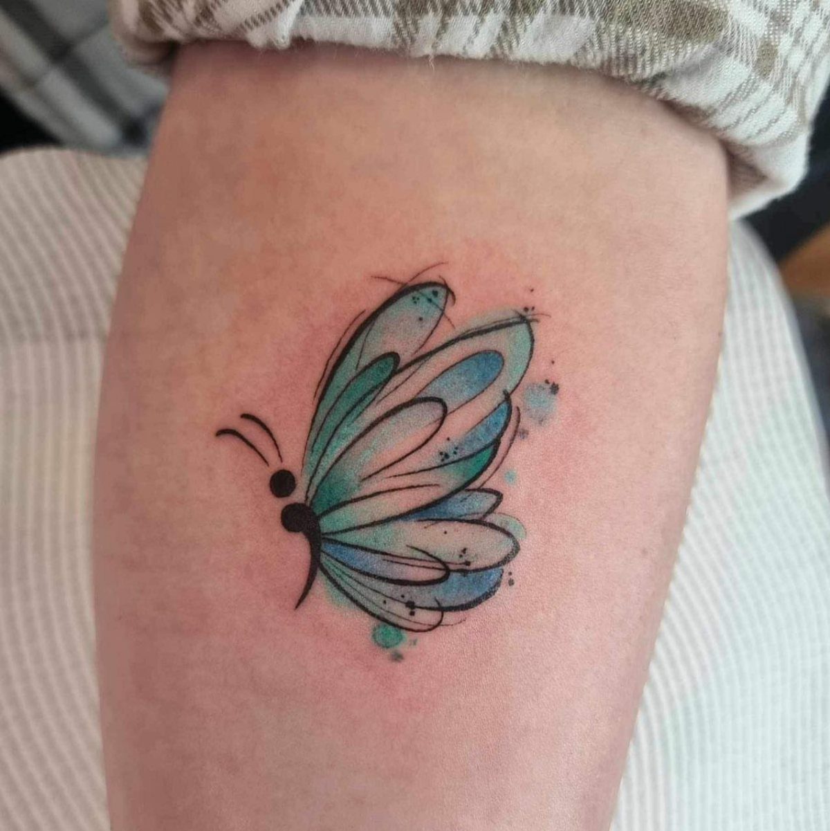 Watercolor butterfly tattoo with a semicolon body in blue and teal ink.