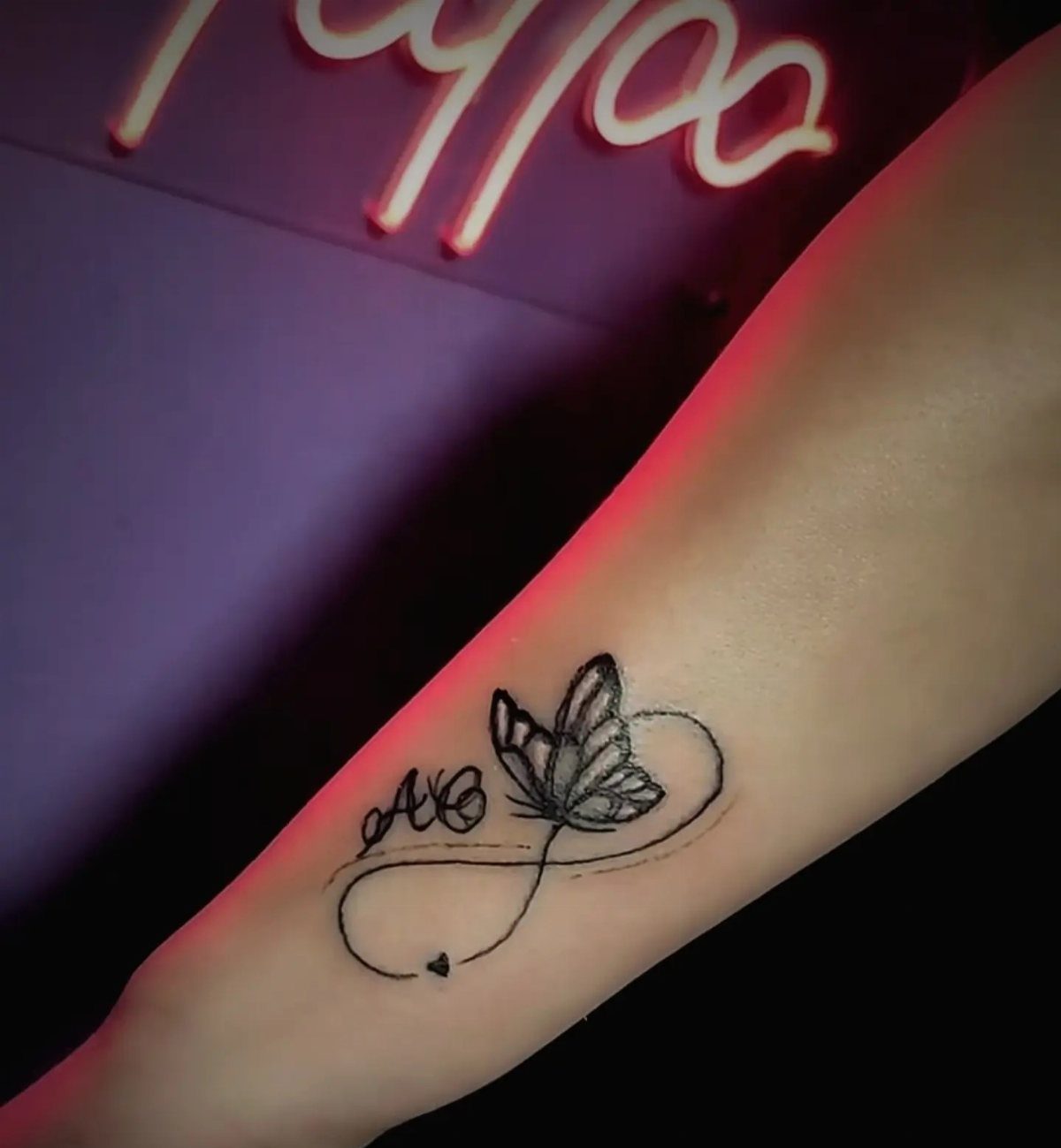 Butterfly tattoo with cursive initials A and C and an infinity symbol loop.