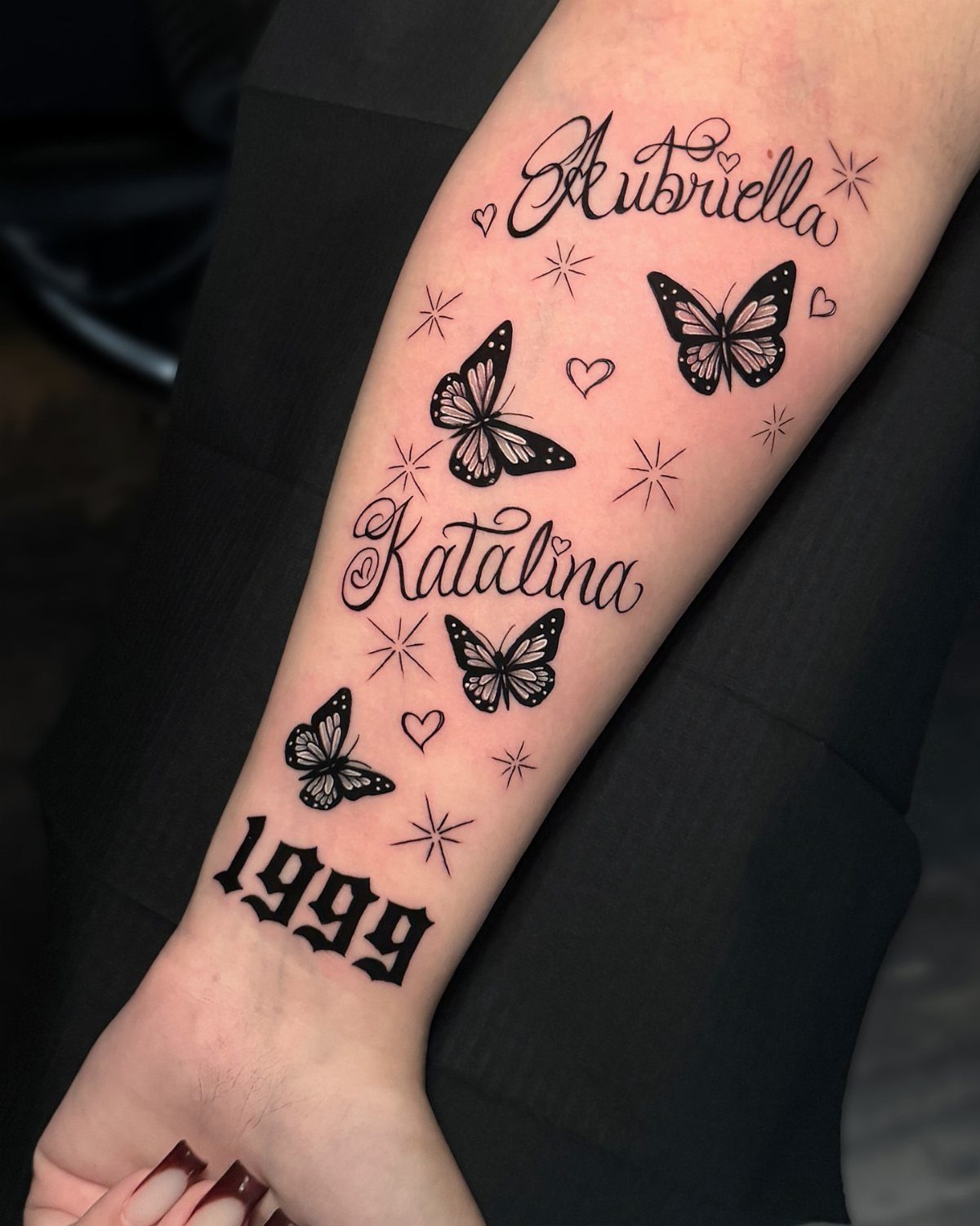 Forearm tattoo featuring three butterflies, the names Aubriella and Katalina, and 1999.