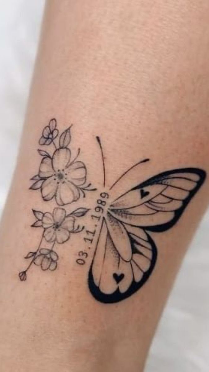 Butterfly wing tattoo with flowers and a date on a person's arm