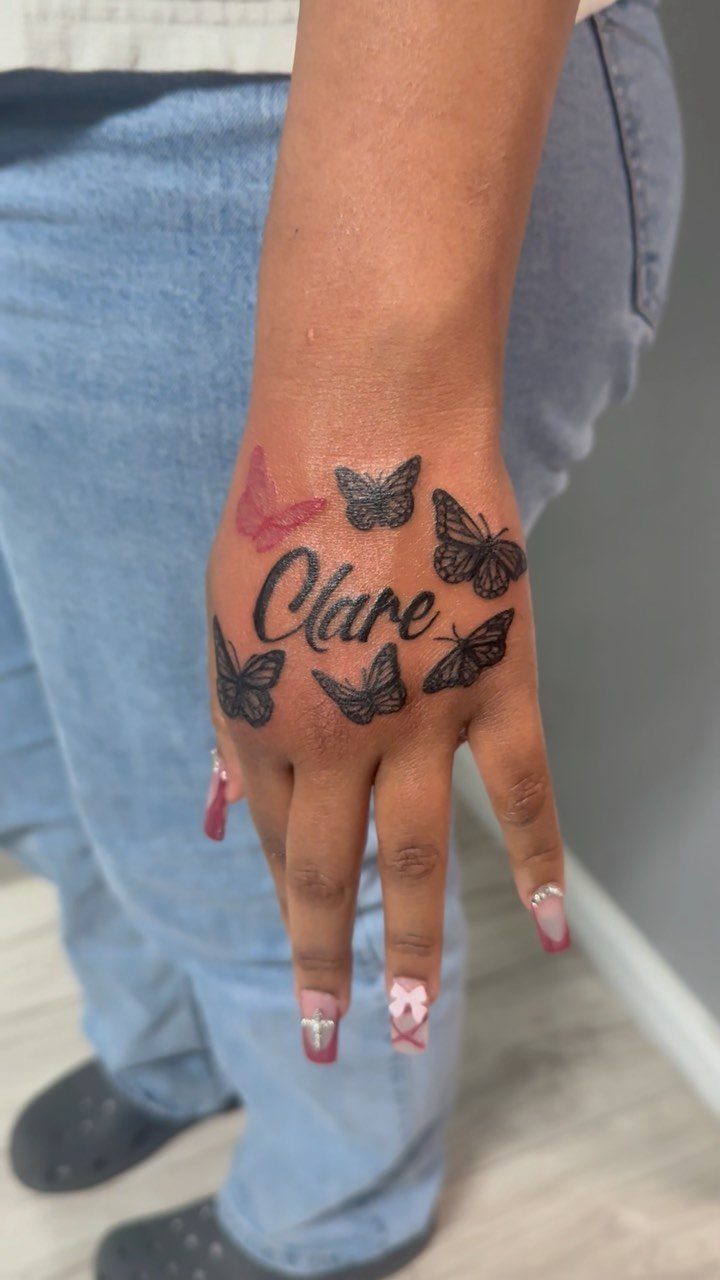Tattoo on a hand showing the name Clare in cursive with butterflies.
