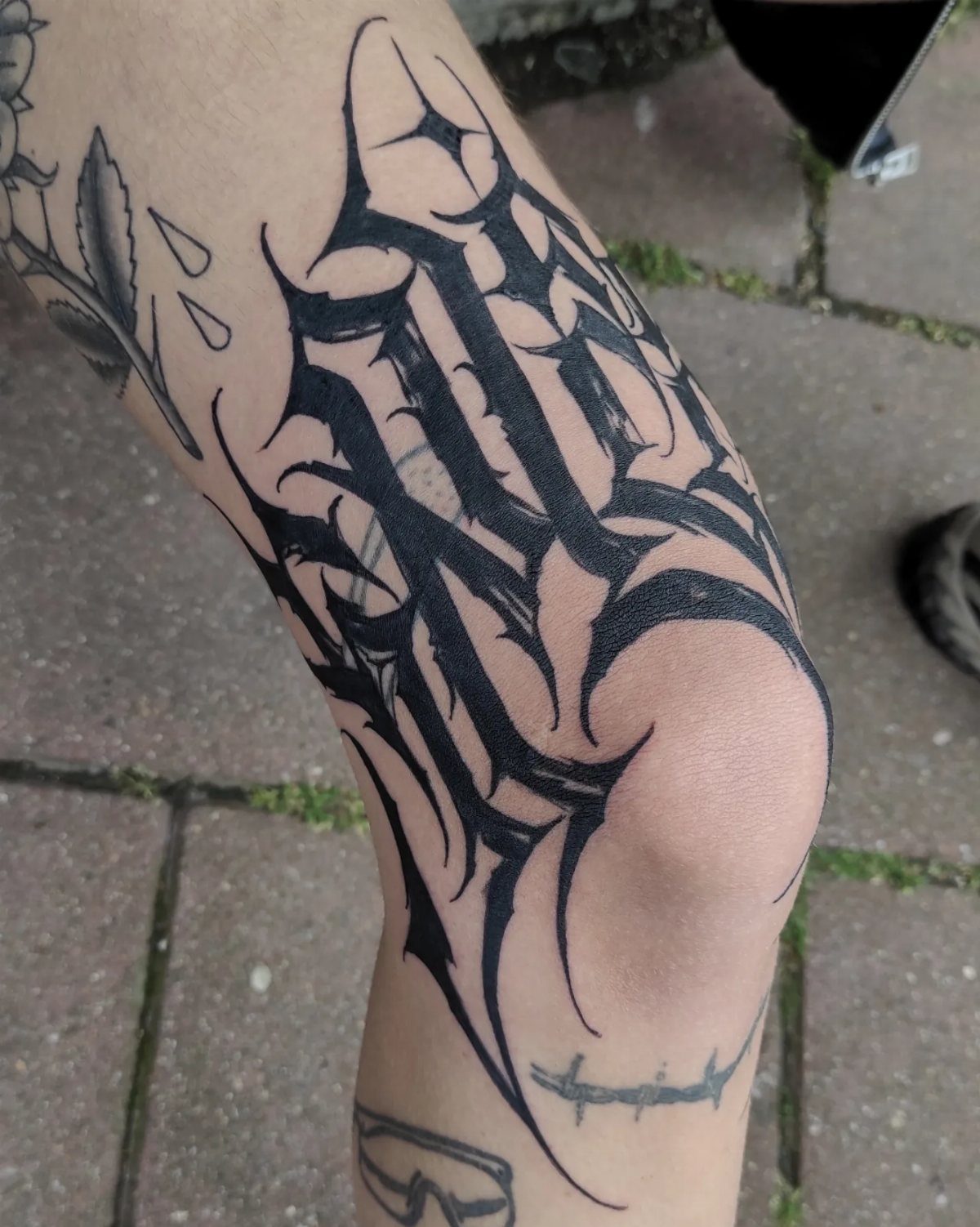 Stylized black ink calligraphy tattoo with sharp edges on a person's leg