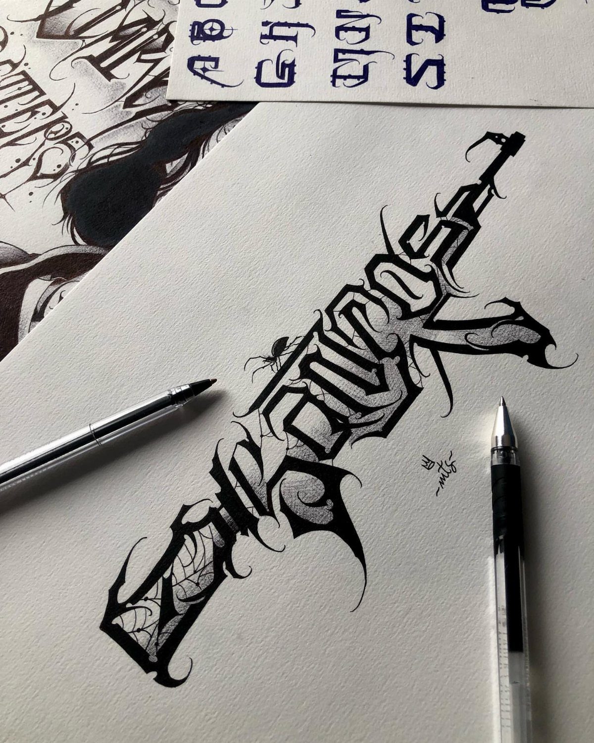 Gothic calligraphy tattoo design drawn in black ink on white paper with pens.