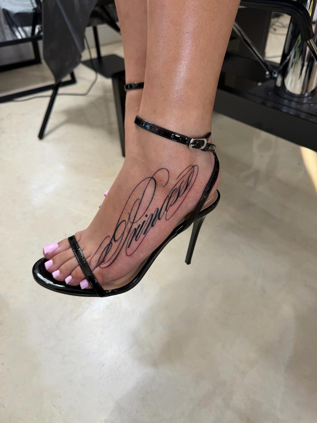 Foot in black high heel with a script tattoo reading Princess in black ink