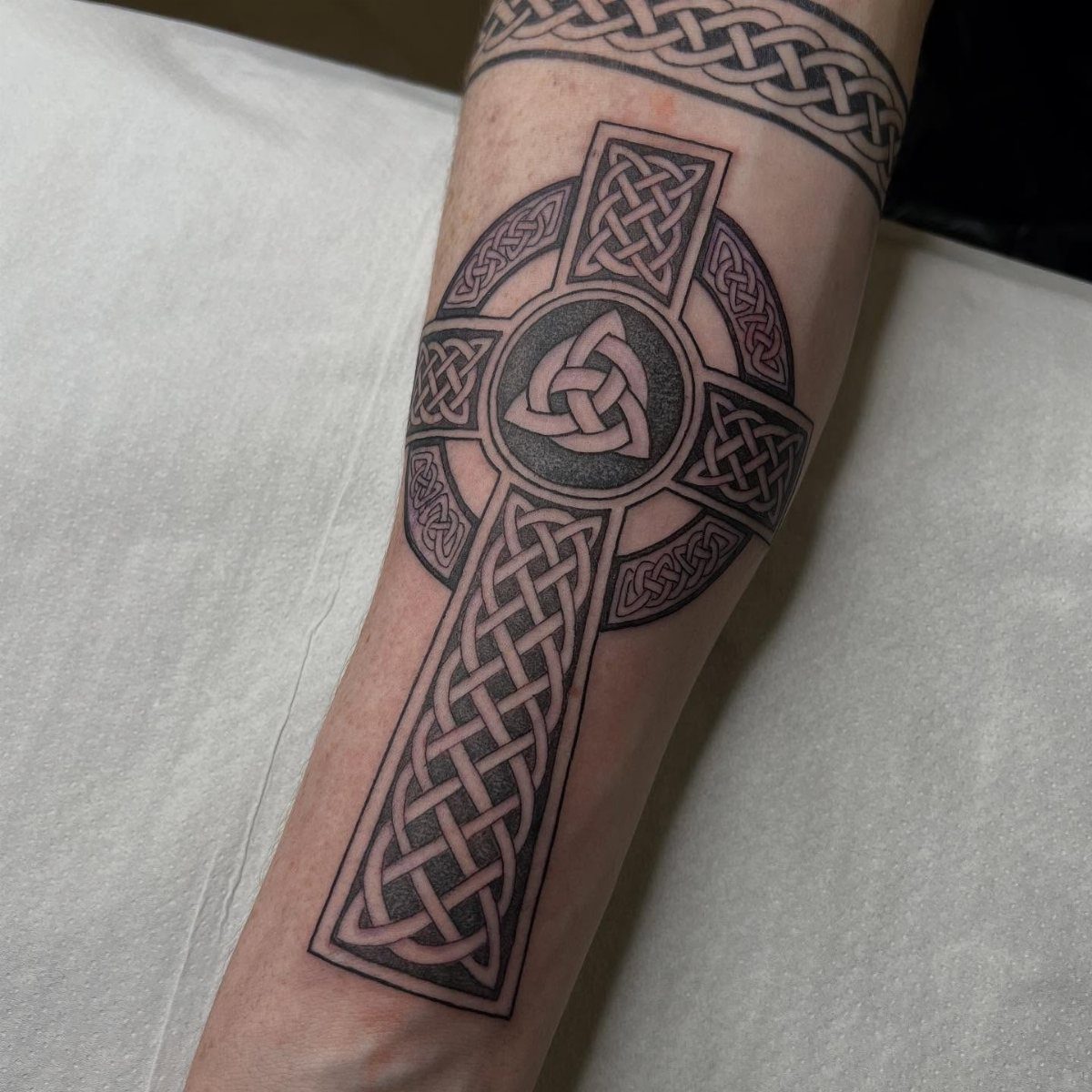 Celtic cross tattoo with intricate knotwork and triquetra on a person's forearm