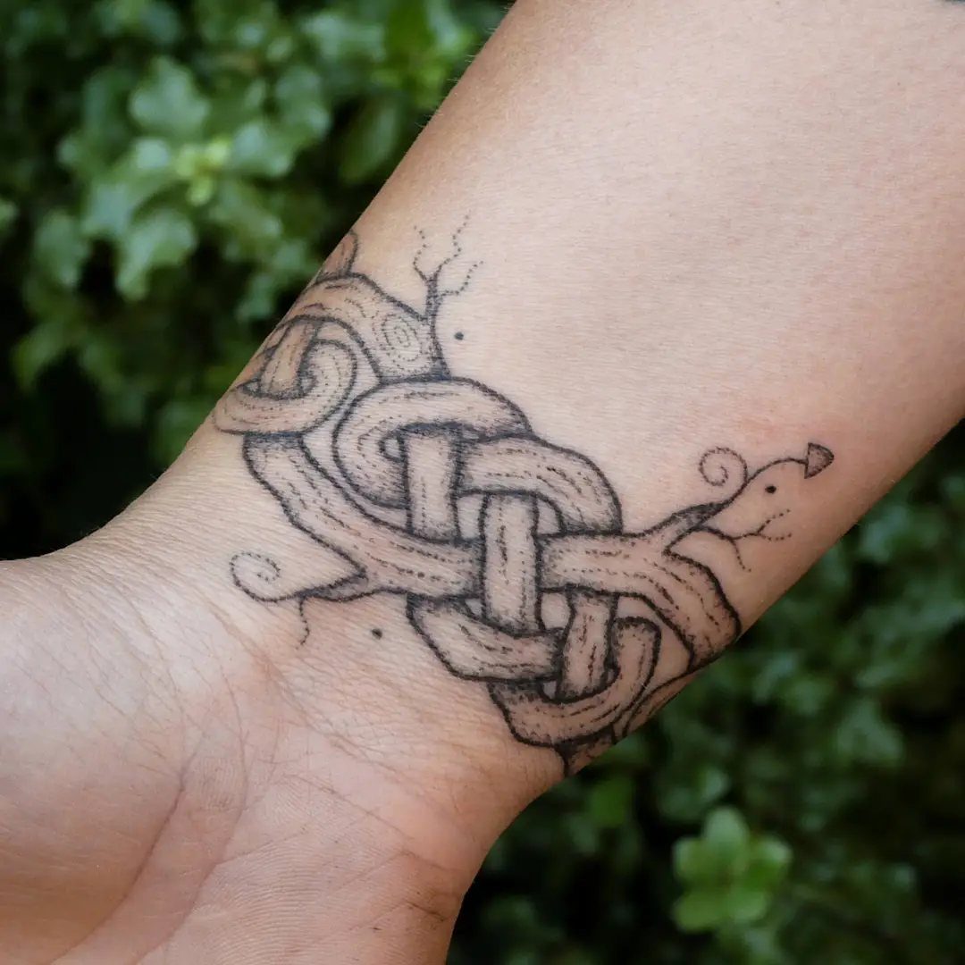 Celtic knot tattoo on a person's wrist with a blurred green leaf background
