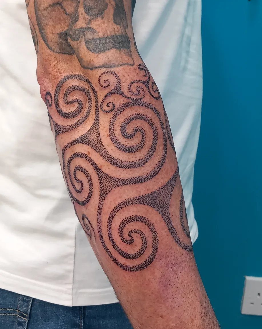 Triple spiral Celtic knot tattoo on a person's forearm using black dotwork technique.