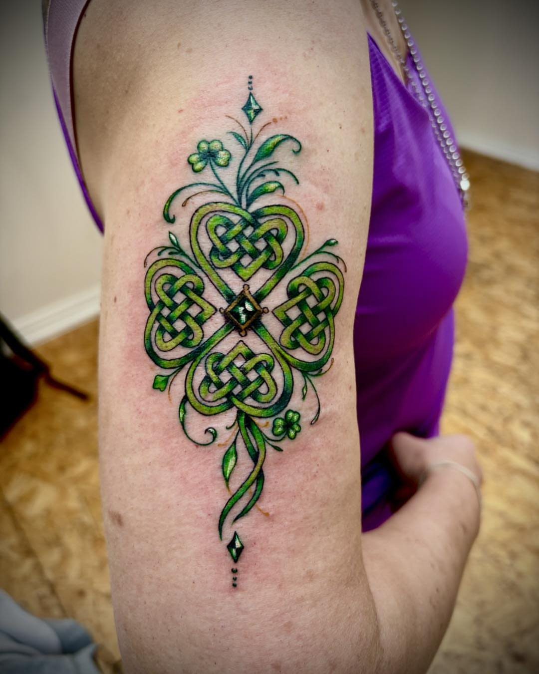 Green Celtic knot tattoo with shamrocks on a person's upper arm