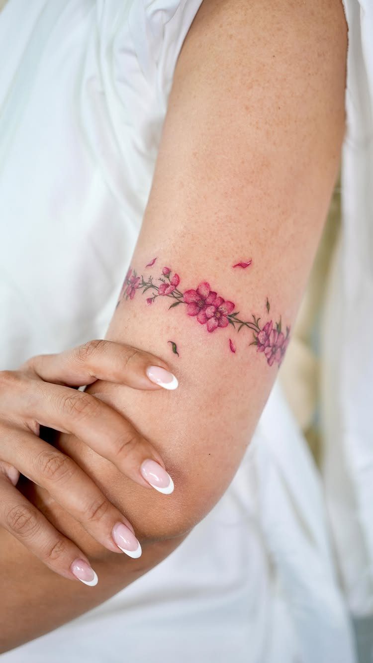 Pink cherry blossom floral tattoo wrapped around a person's upper arm