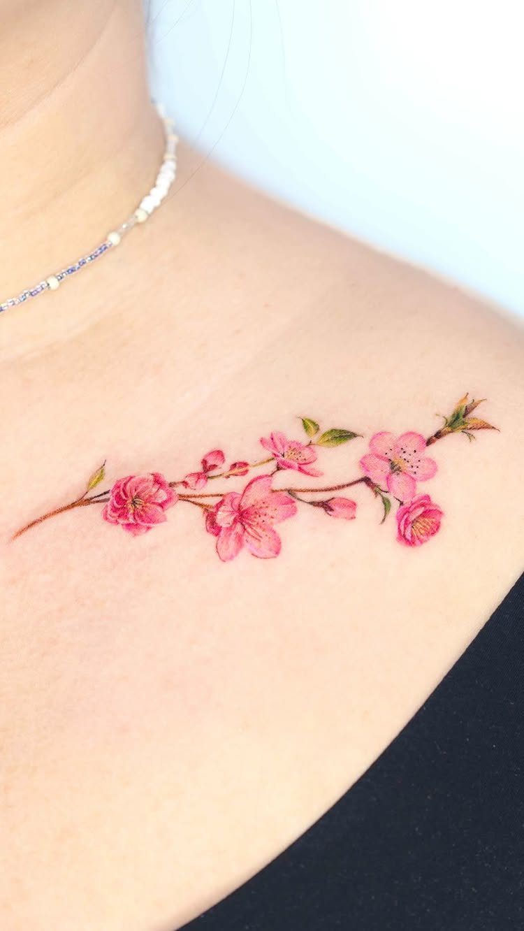 Cherry blossom branch tattoo with pink flowers on a person's collarbone and shoulder.