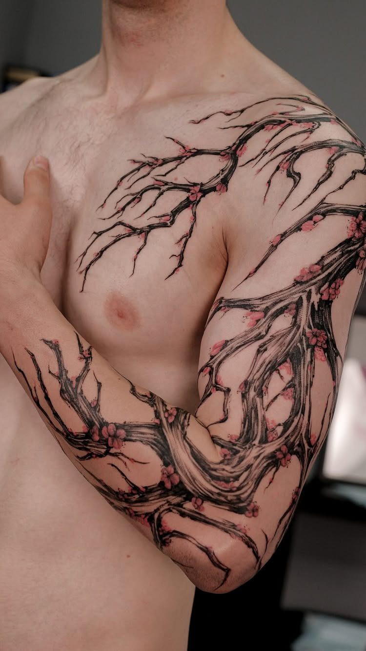 Cherry blossom branch tattoo extending across a man's chest, shoulder, and arm.