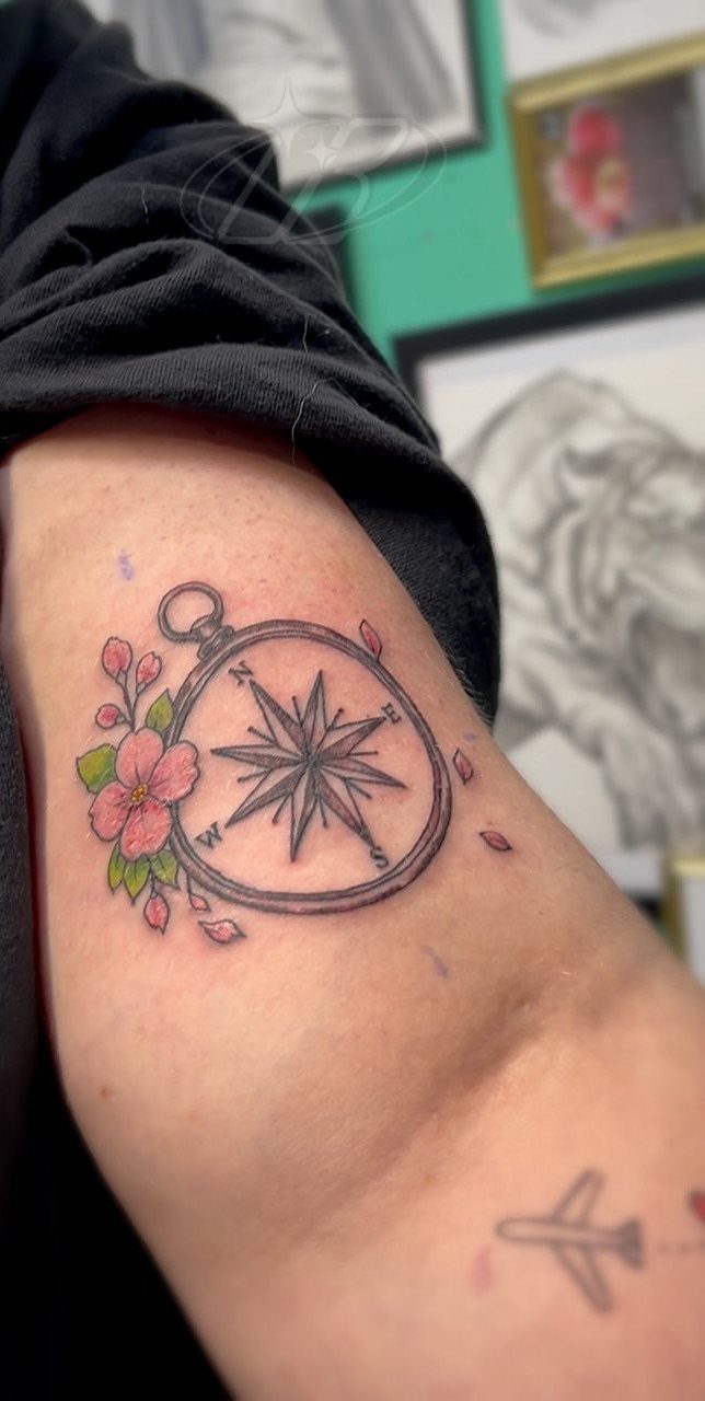 Compass tattoo with pink cherry blossoms and petals on a person's upper arm