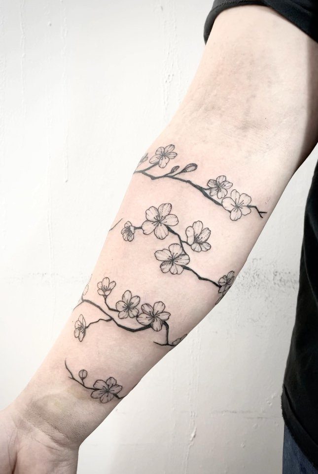 Cherry blossom branch tattoo wrapping around a person's forearm in black ink.