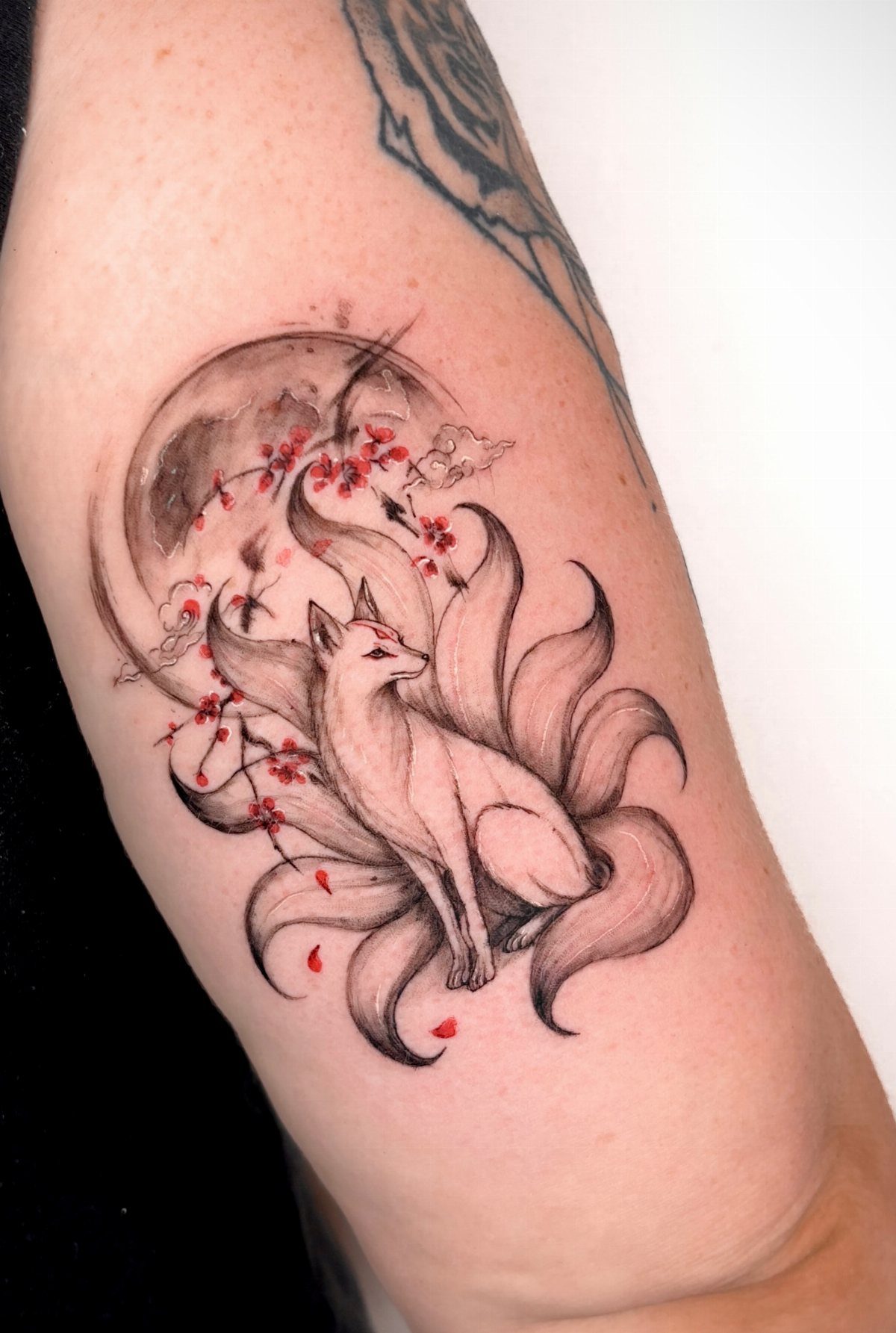 Multi-tailed white fox tattoo with pink cherry blossoms and a moon on skin