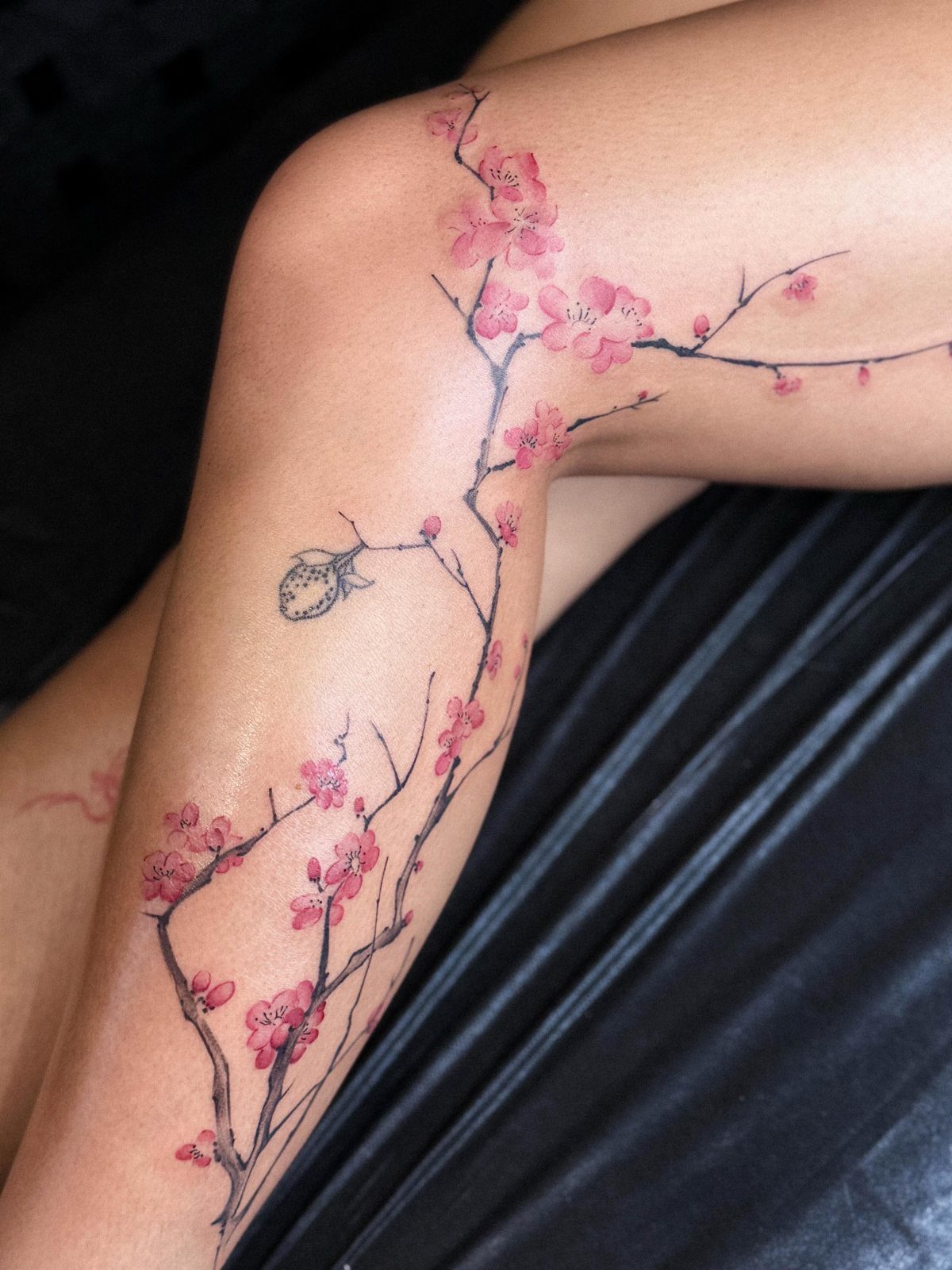 Cherry blossom branch tattoo with pink flowers on a person's leg and knee