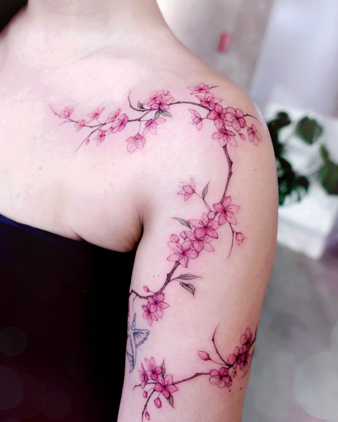 Pink cherry blossom tattoo winding across a person's shoulder and upper arm.