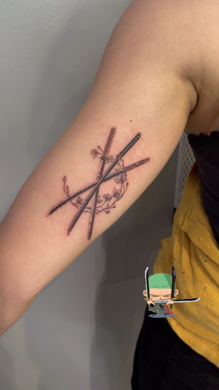 Tattoo on an arm showing crossed swords surrounded by a cherry blossom wreath.