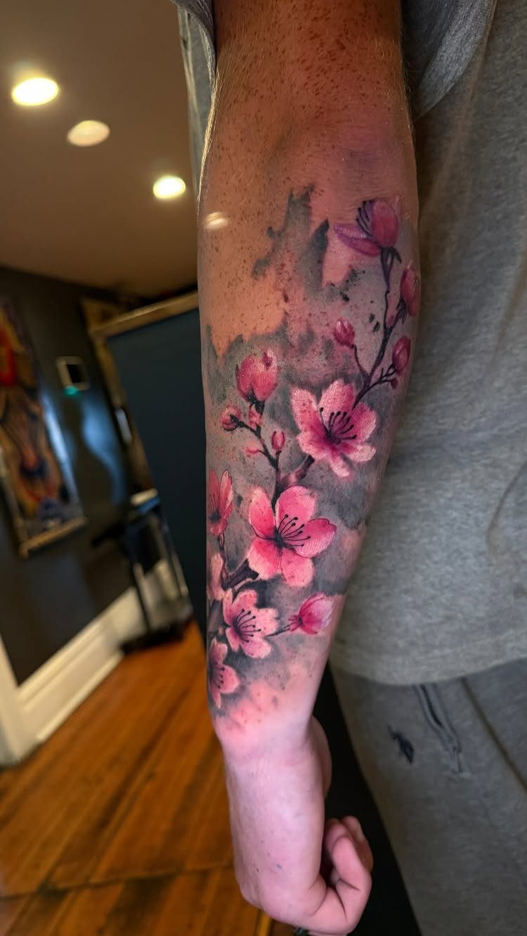 Pink cherry blossom tattoo with watercolor effects on a person's forearm