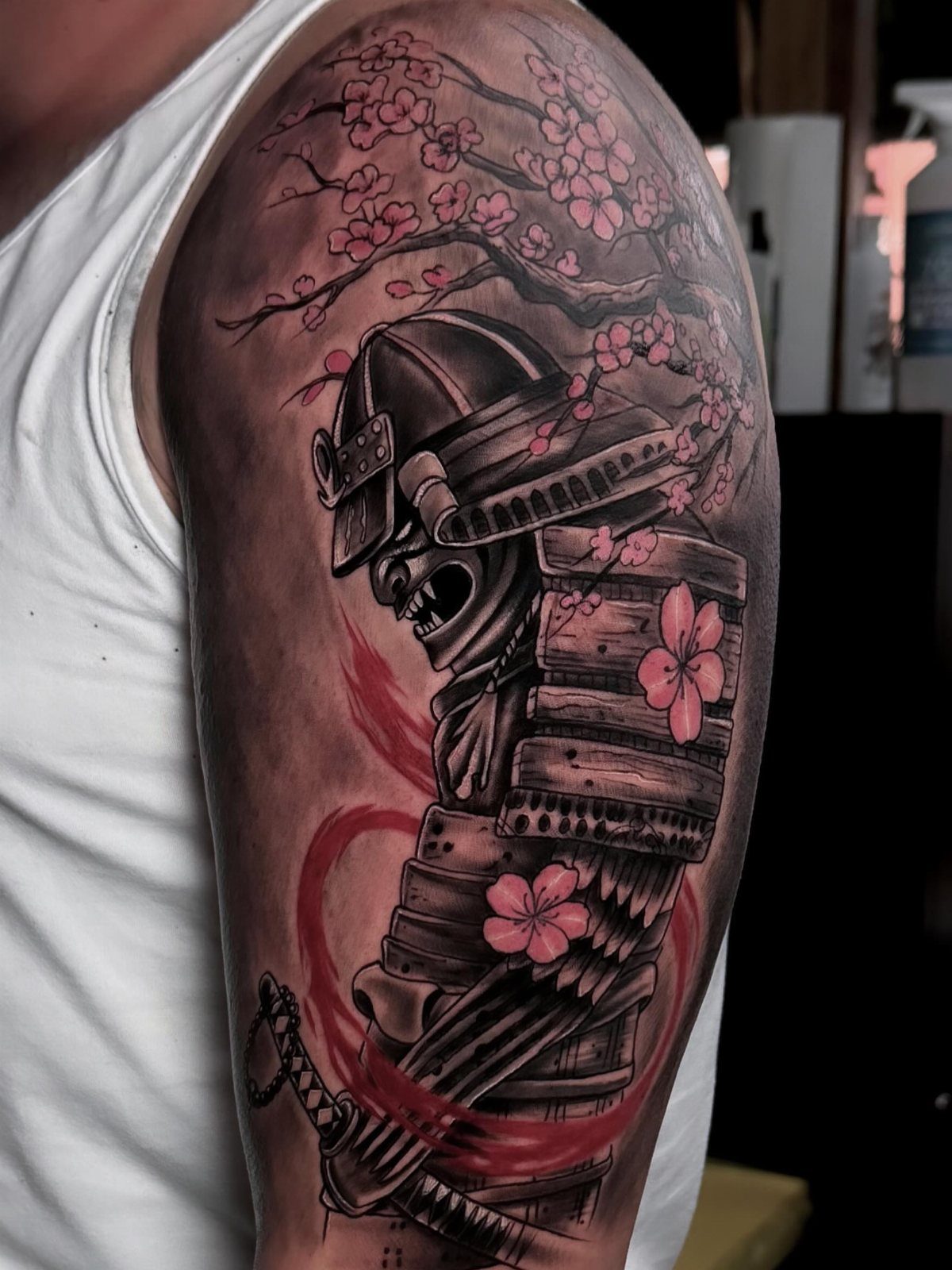 Samurai armor tattoo with pink cherry blossoms on a person's upper arm