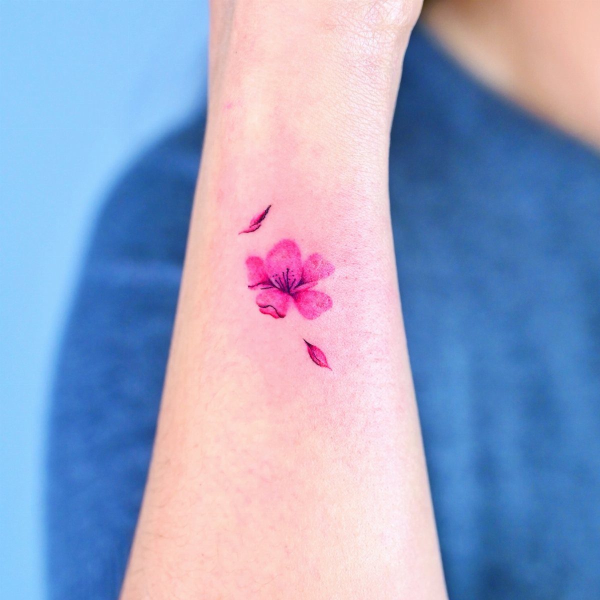 Pink cherry blossom flower tattoo with two petals on a person's inner forearm.