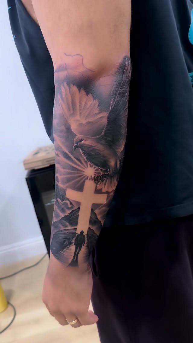 Forearm sleeve tattoo featuring a glowing cross, a dove, and mountain scenery.