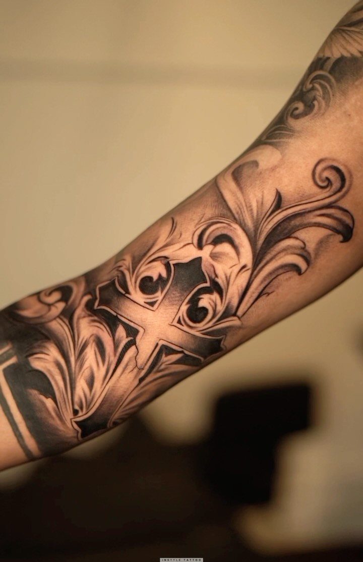 Sleeve tattoo featuring a cross surrounded by ornate floral and leaf scrollwork designs.