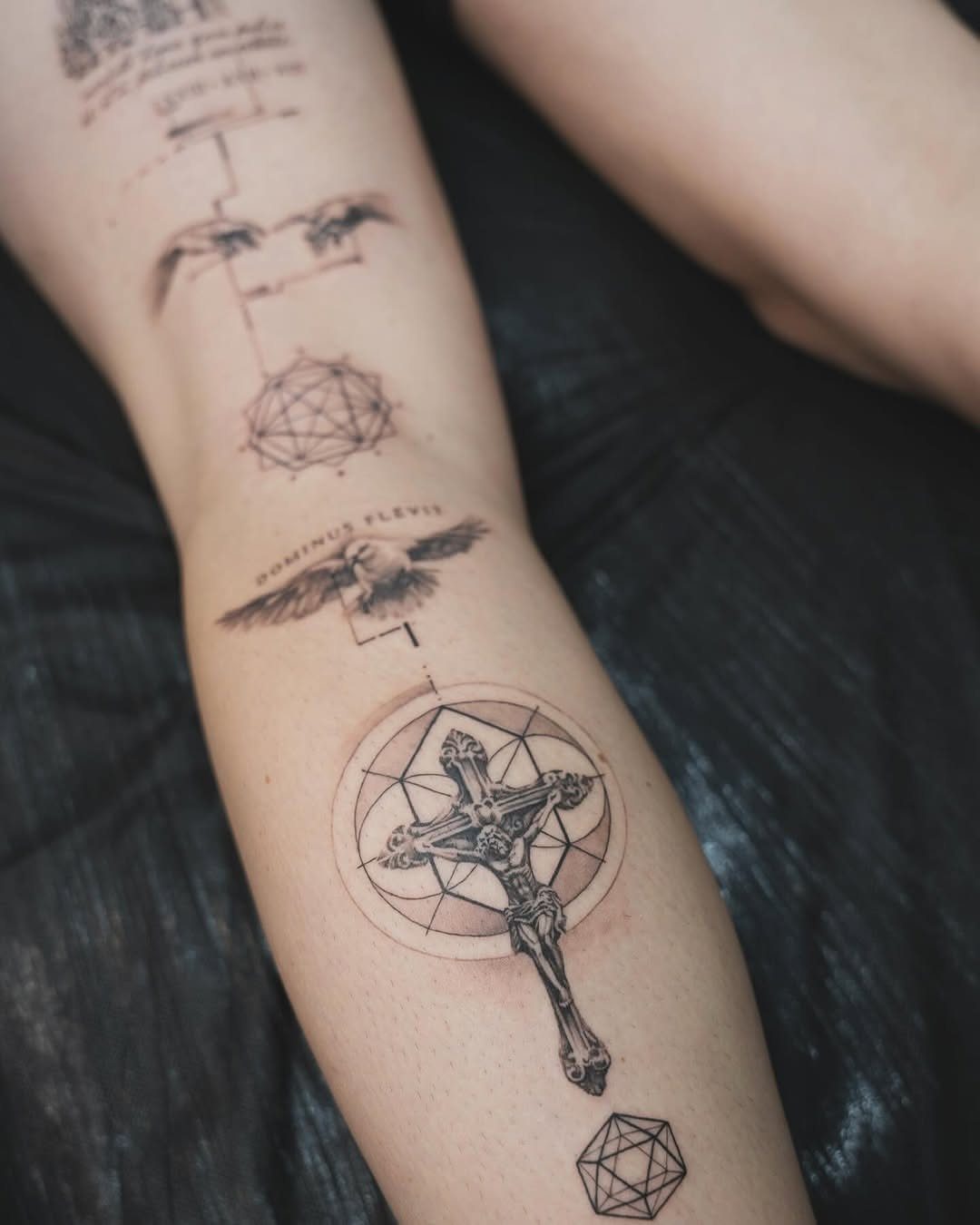 Tattooed arm showing a crucifix and dove combined with geometric shapes and lines.