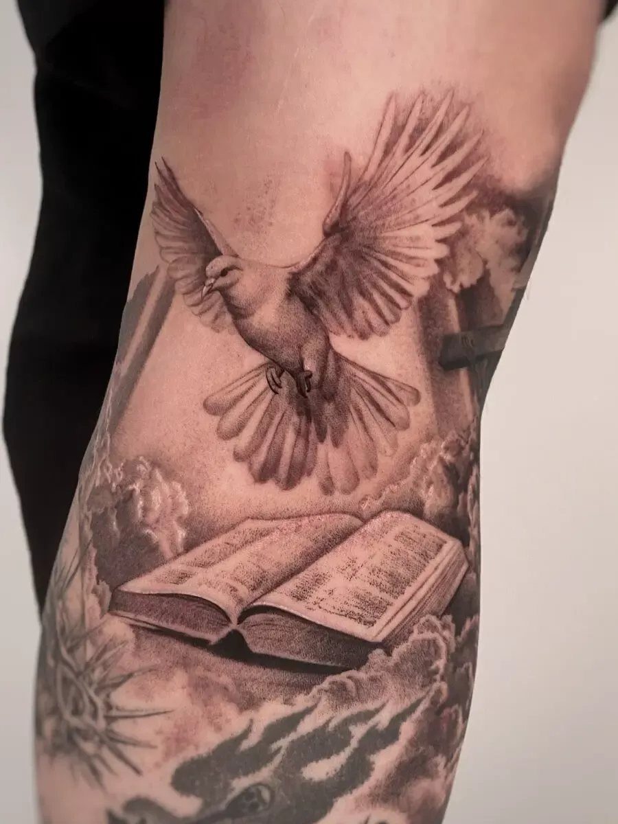 Tattoo of a flying dove above an open Bible on a person's arm