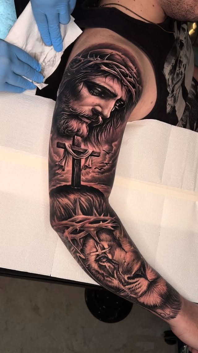 Jesus sleeve tattoo with a crown of thorns, cross, and lion on arm