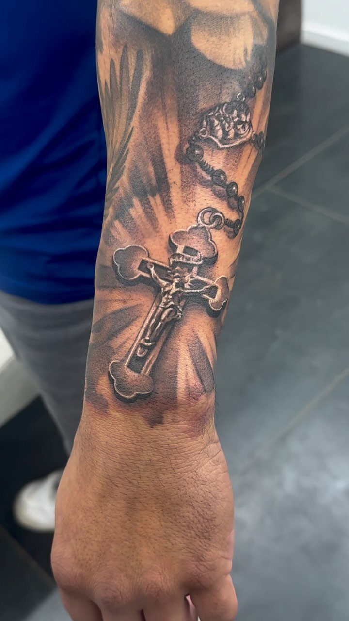 Rosary tattoo with a crucifix and radiating light on a man's forearm.