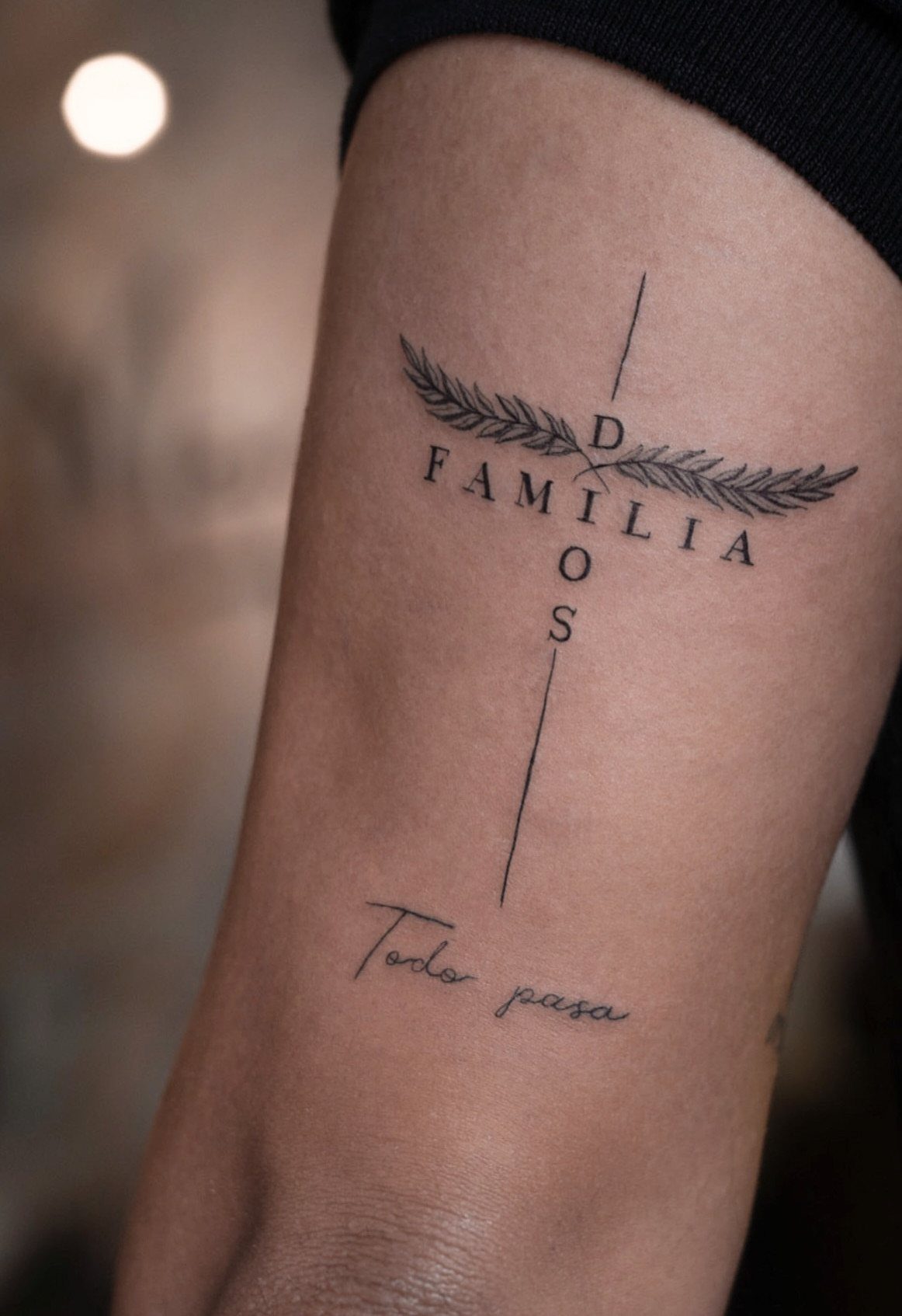 Minimalist cross tattoo on a forearm with the word FAMILIA and cursive text.
