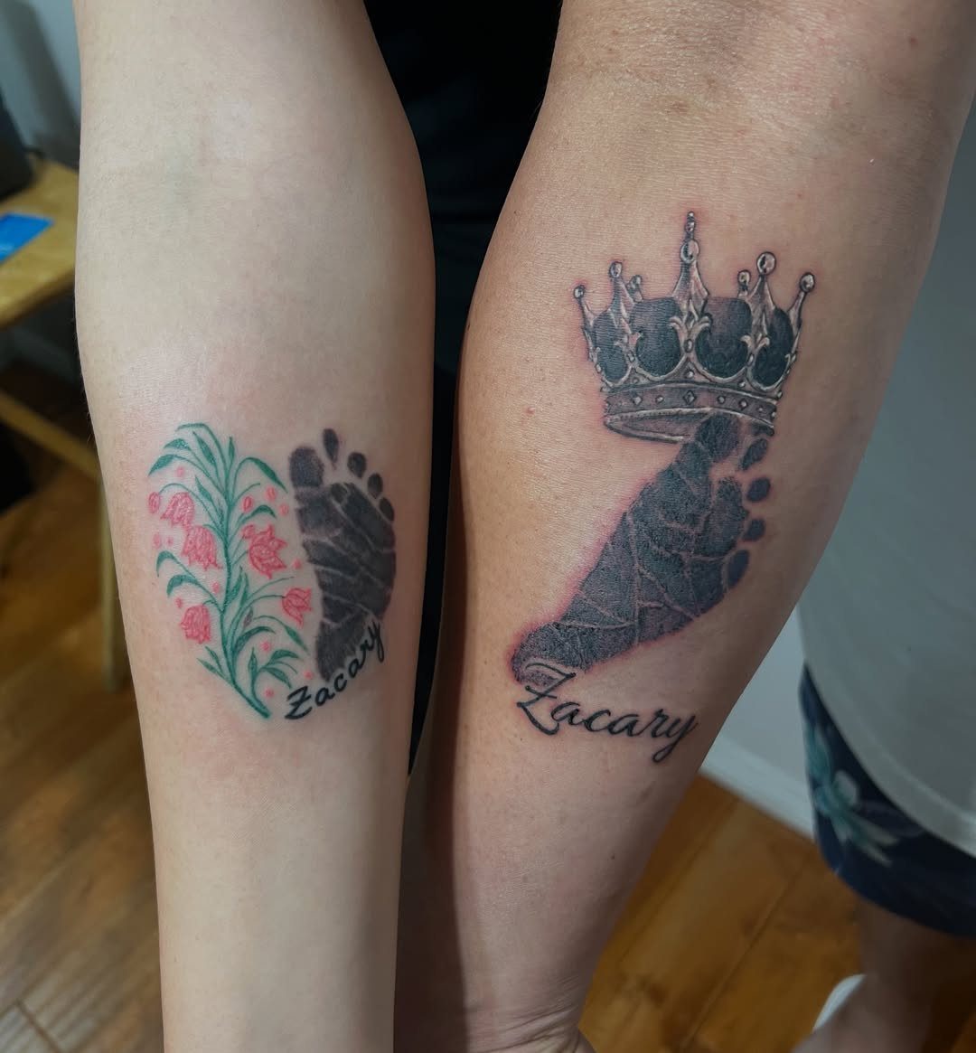 Two forearms with matching baby footprint tattoos and the name Zacary.
