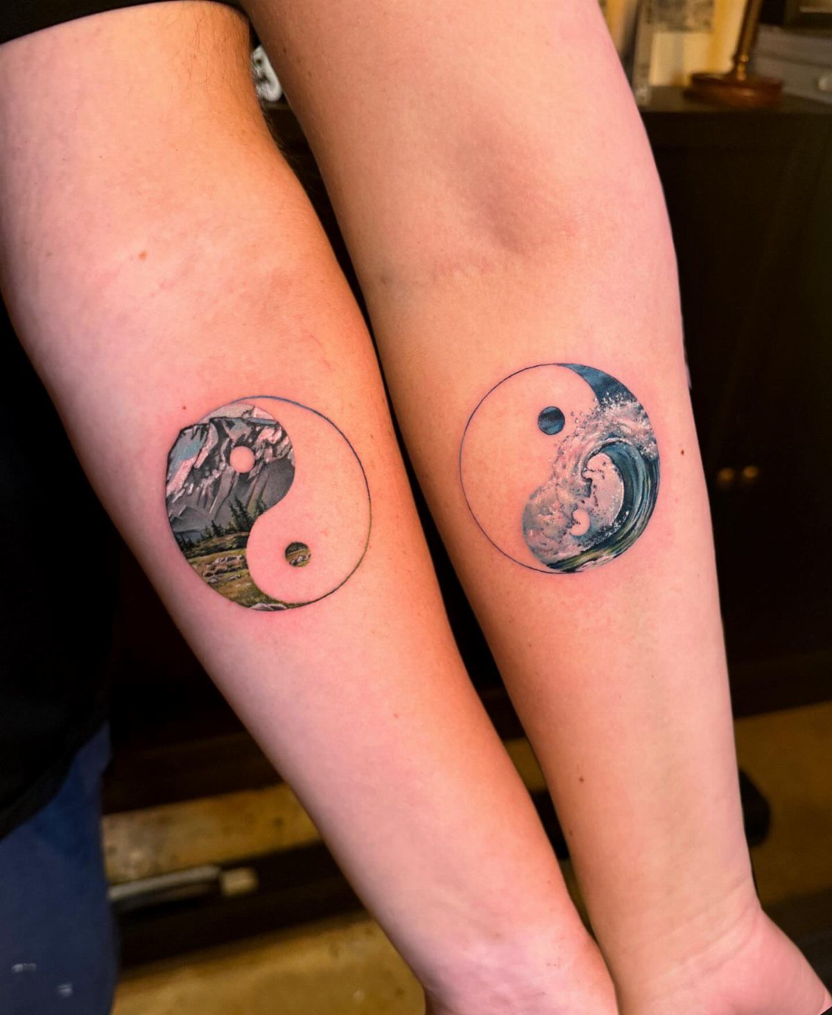 Two forearms with matching yin-yang tattoos featuring a mountain and an ocean wave.