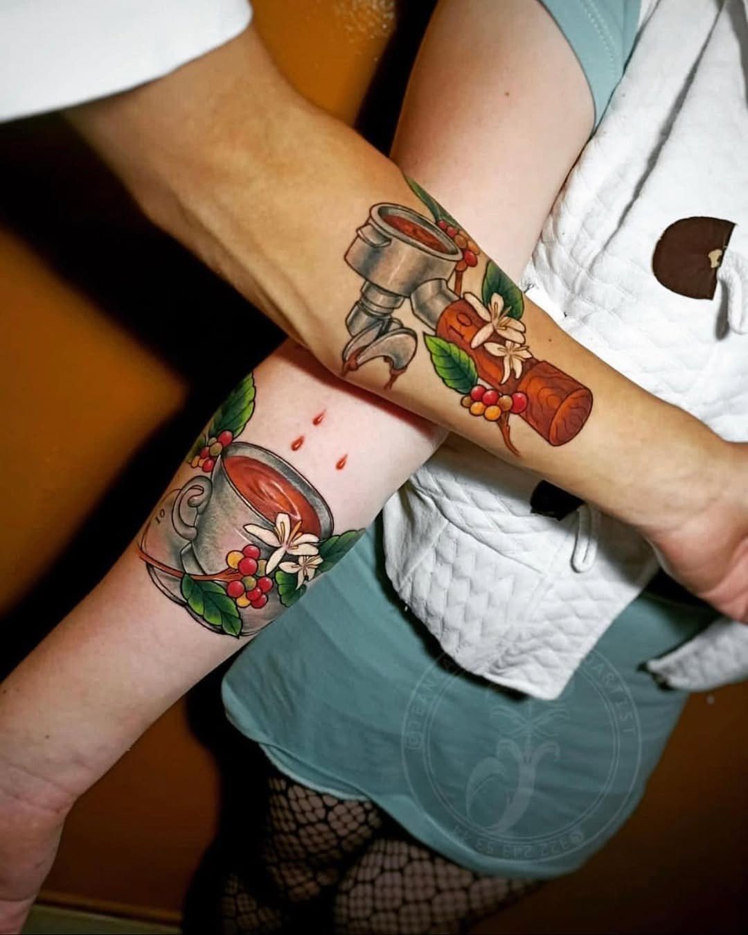 Two forearms with matching coffee-themed tattoos of a coffee cup and a tamper.