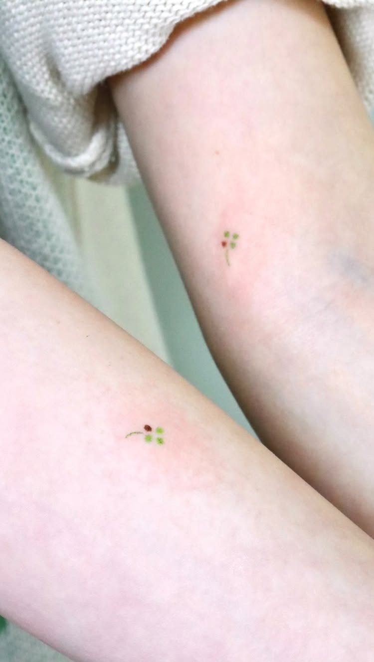 Two arms with matching small four-leaf clover tattoos in green and red.