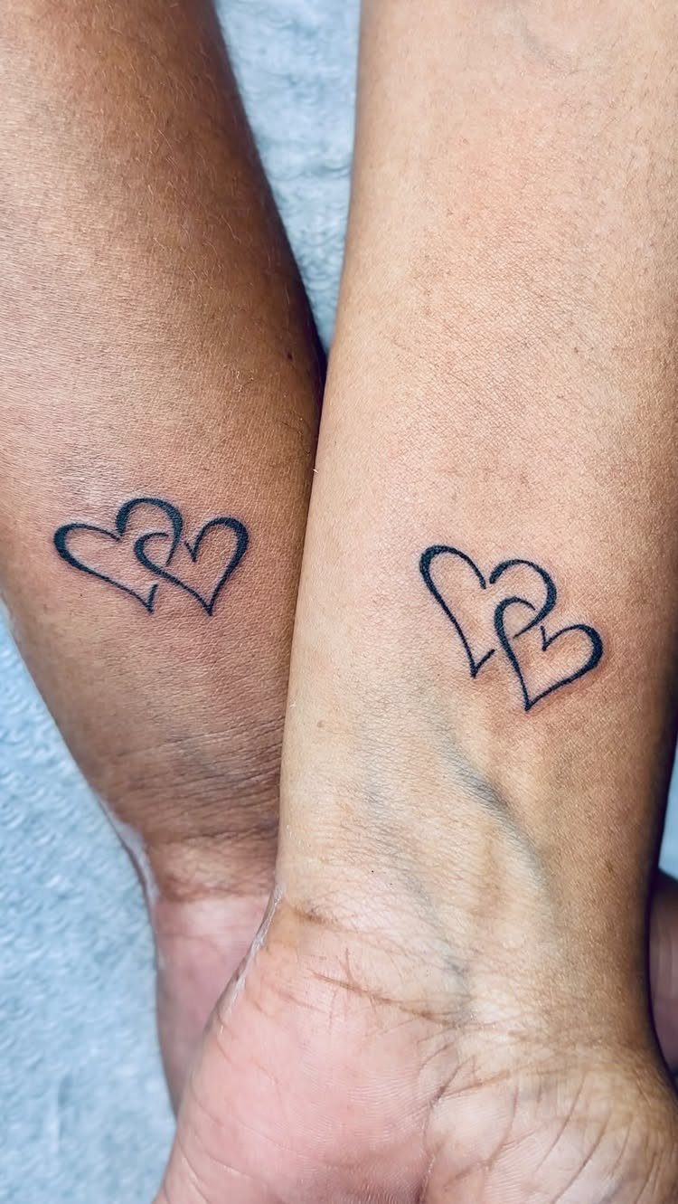 Two interlocking heart tattoos on the inner wrists of a couple.