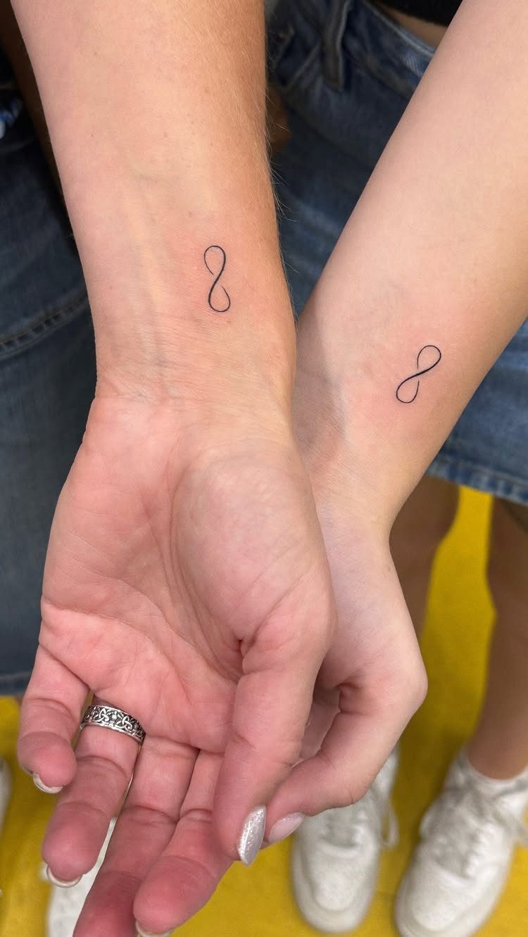 Two inner wrists each featuring a small black infinity symbol matching tattoo.